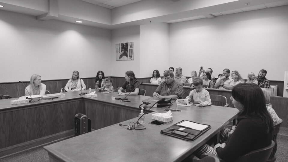 Group of people seated in a courtroom, engaged in discussion, in black-and-white.