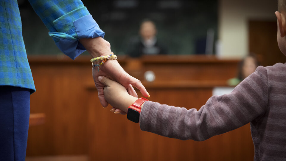 Child holding hand with adult in a courtroom